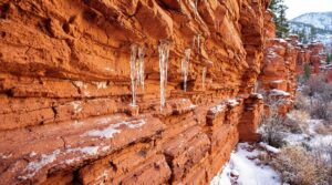 Close-up of weathered sandstone wall with cracks, icicles, and frost, showing effects of freeze-thaw cycles in winter.